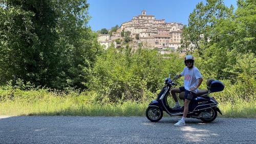 Vespa tour through the rolling hills of Le Marche.Medieval hilltop village with fortifications.Charming narrow streets in an old Italian town.Scenic view from a castle walkway.Village surrounded by nature, forests, and hills.Ancient castle with stone walls and towers.Panoramic road winding through the Marche countryside.