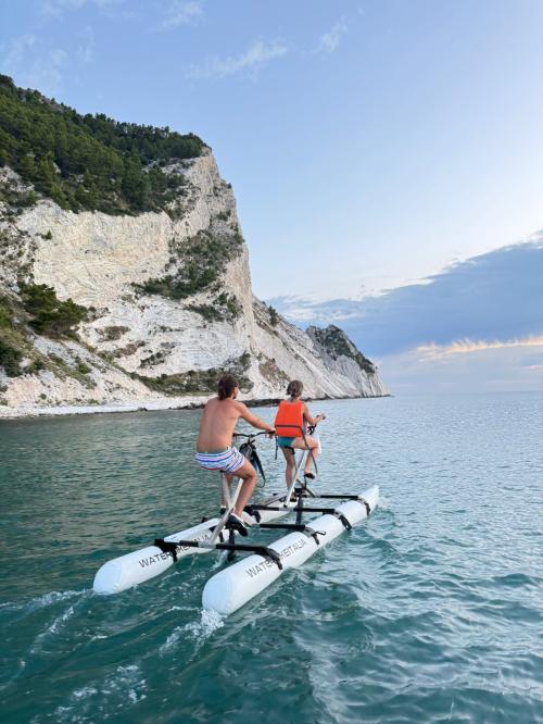 Persona in waterbike lungo la costa della Riviera del ConeroWaterbike su acqua cristallina con sfondo di scogliere biancheAlba vista dalla waterbike a largo del ConeroGruppo di persone in escursione waterbike vicino alla Spiaggia delle Due SorelleTramonto dorato sulla Riviera del Conero visto da una waterbikeVista panoramica della costa marchigiana da una waterbike in mareTour guidato in waterbike con paesaggi naturali mozzafiatoDettaglio di una waterbike galleggiante sull'acqua limpida del Conero